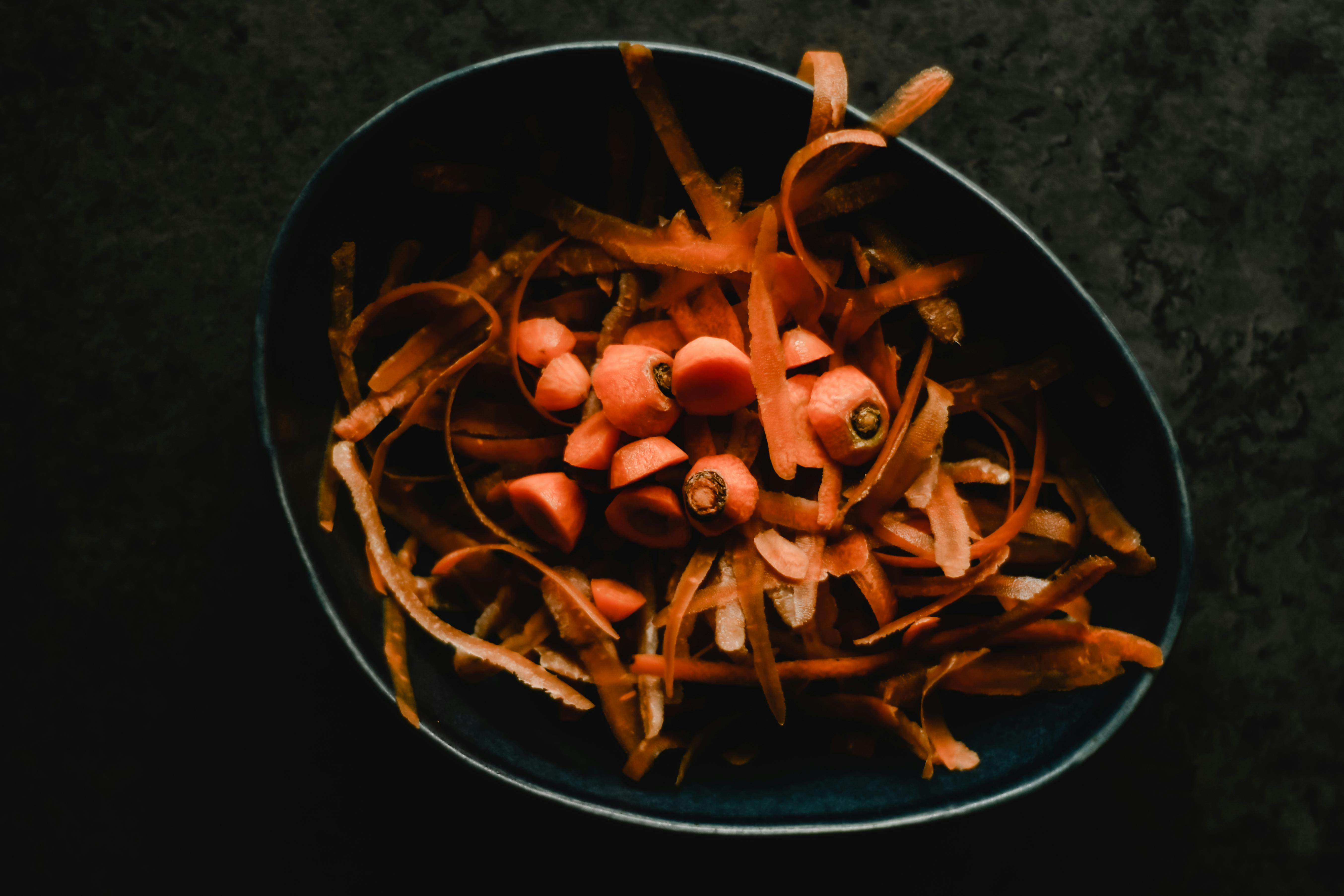 Dark ceramic bowl filled with organic carrot peelings and tops, suitable for composting or broth making.