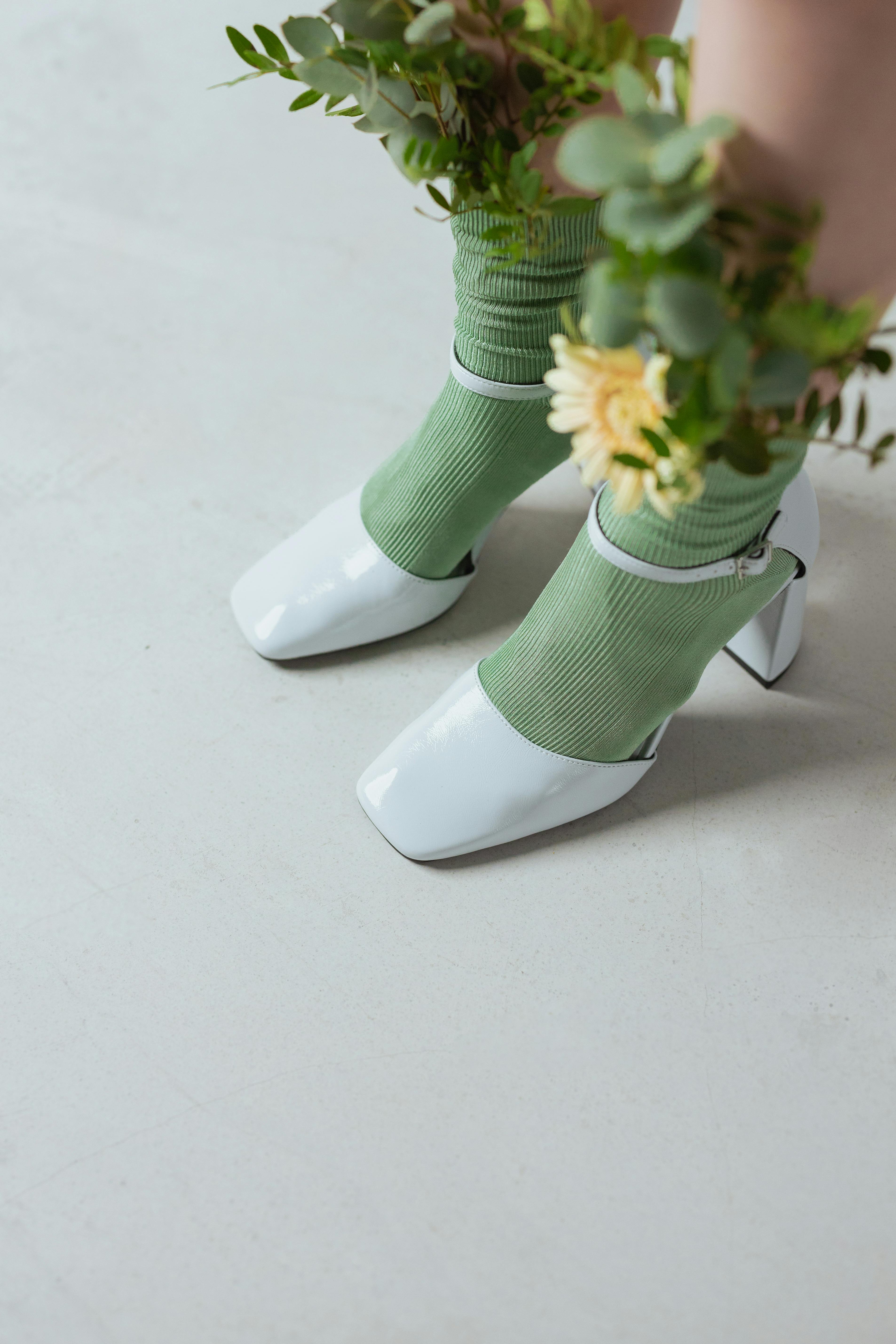White patent leather heels worn over green socks with flowers and foliage tucked in.